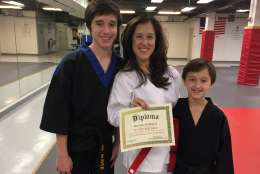 Melissa Marquez shows off her black belt sons, and the red belt diploma she earned. (WTOP/Michelle Basch)