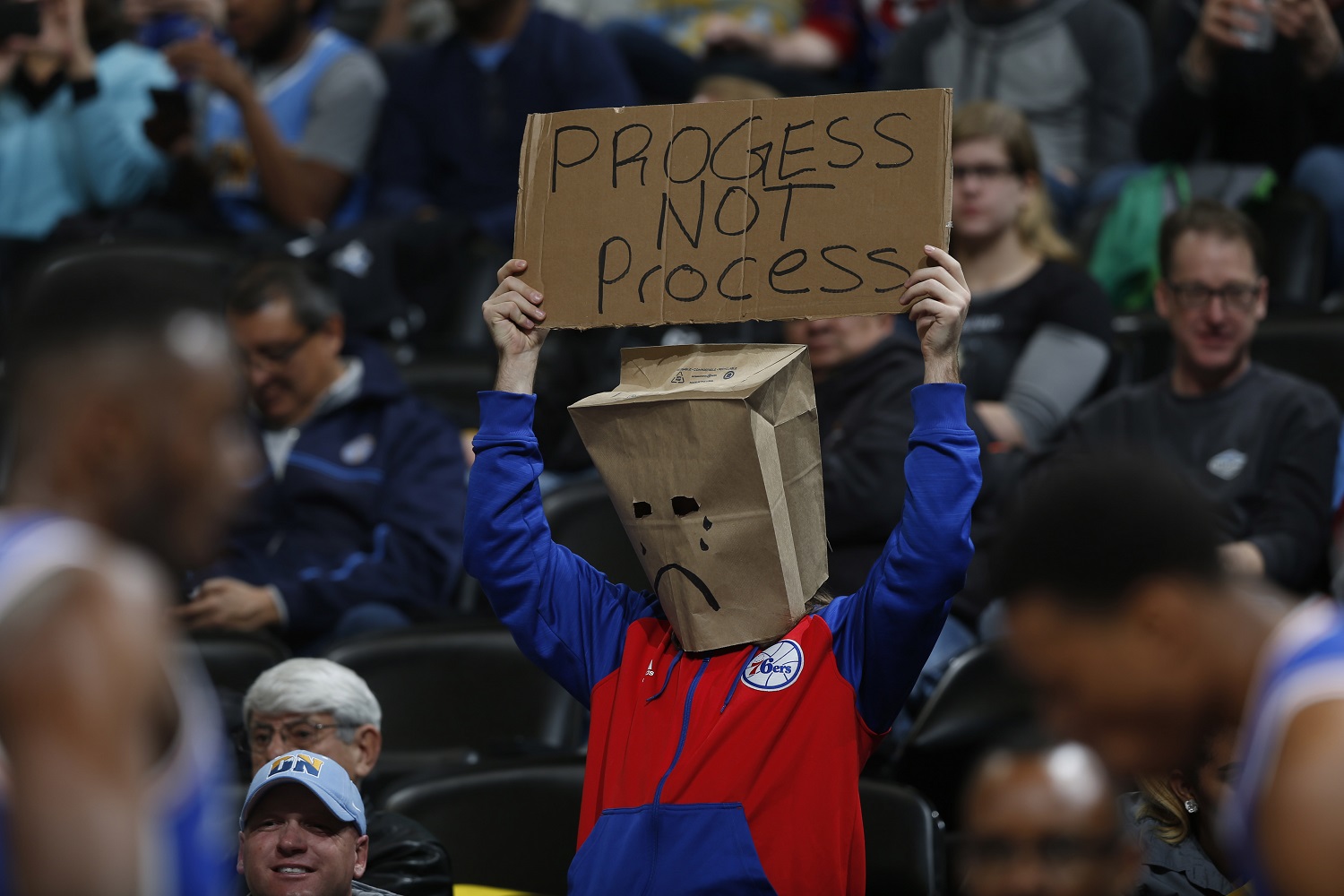 A Philadelphia 76ers fan wears a bag over his head and holds up a placard while watching his team face the Denver Nuggets in the first half of an NBA basketball game Wednesday, March 23, 2016, in Denver. (AP Photo/David Zalubowski)