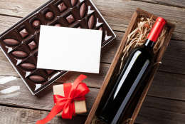 Valentines day greeting card. Red wine, gift box and chocolate box on wooden table. Top view with space for your greetings