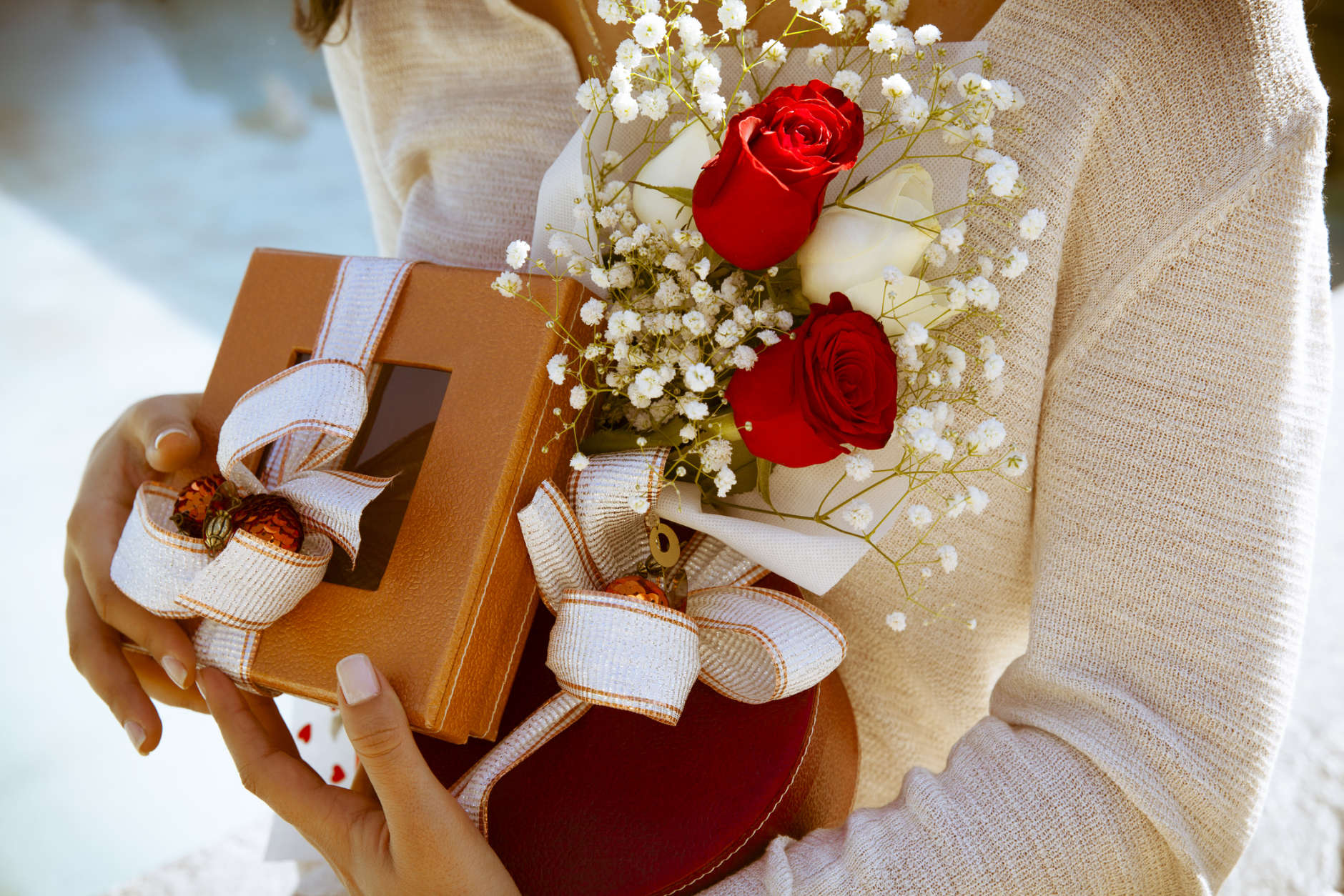 Close up shot of female hands holding gifts wrapped with white ribbon and bouquet of red roses. Time for gifts. Shallow depth of field with focus on gifts.Outdoors shot, Horizontal