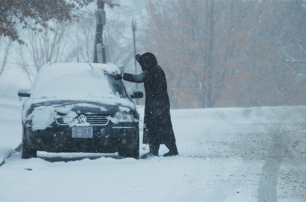 A woman sweeps wet snow off a car in Northwest Washington during a heavy snowfall in early March -- yes, March -- 2015. (WTOP/Dave Dildine)