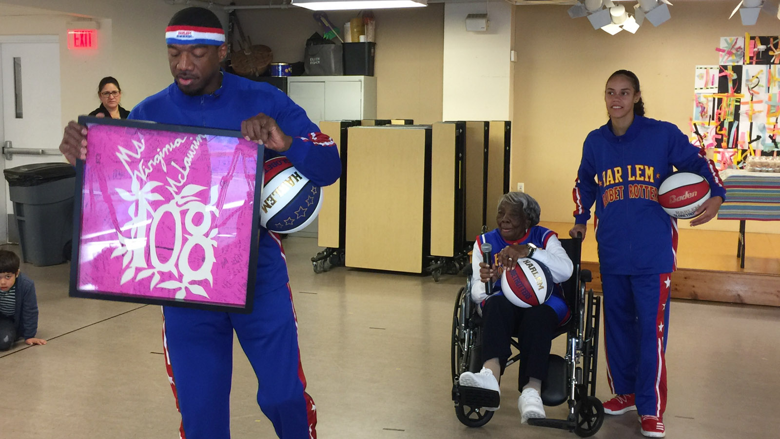 Harlem Globetrotter Buckets Blakes holds a framed card signed by every student at LAMB Public Charter School in Northwest. Virginia McLaurin said her apartment is full of flowers and cards from her 108th birthday celebration on Sunday.(WTOP/Kristi King)