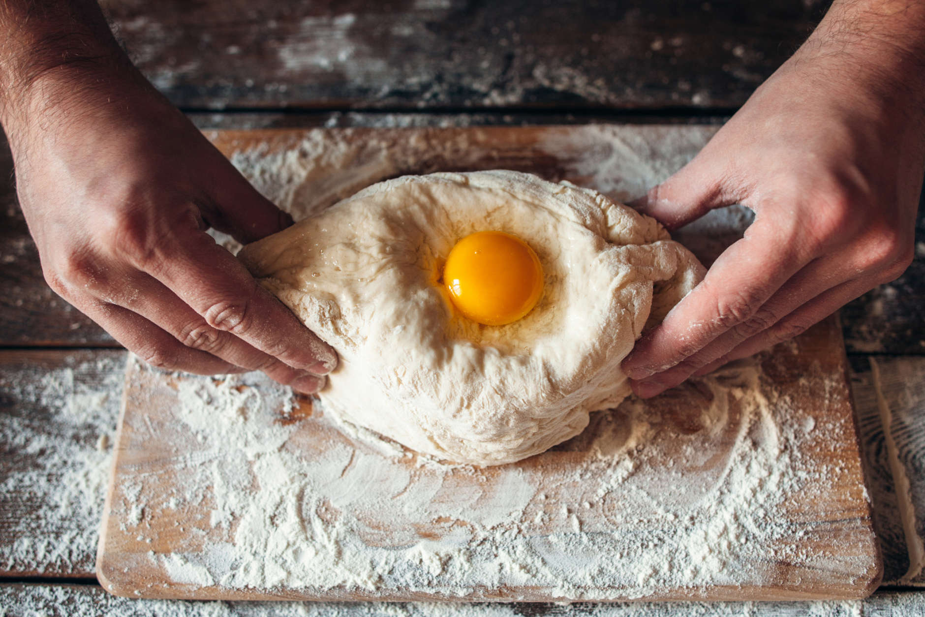 Baker hands preparing khachapuri on kitchen table. Top view on cook making traditional georgian treat with raw dough and egg. Culinary, cooking, recipe concept