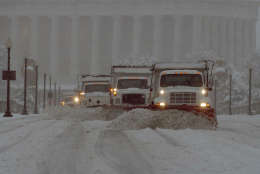 A line of trucks with snow plows push snow across the Memorial Bridge heading from Washington into Arlington, Va. as snow fell in the Washington area, March 13, 1993. The major storm battered the area snarling roads and closing museums. The Lincoln Memorial is in the background. (AP Photo/Mark Wilson)