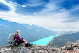 Young tourist woman is feeling free and sitting on the top of the mounting and looking at a beautiful landscape