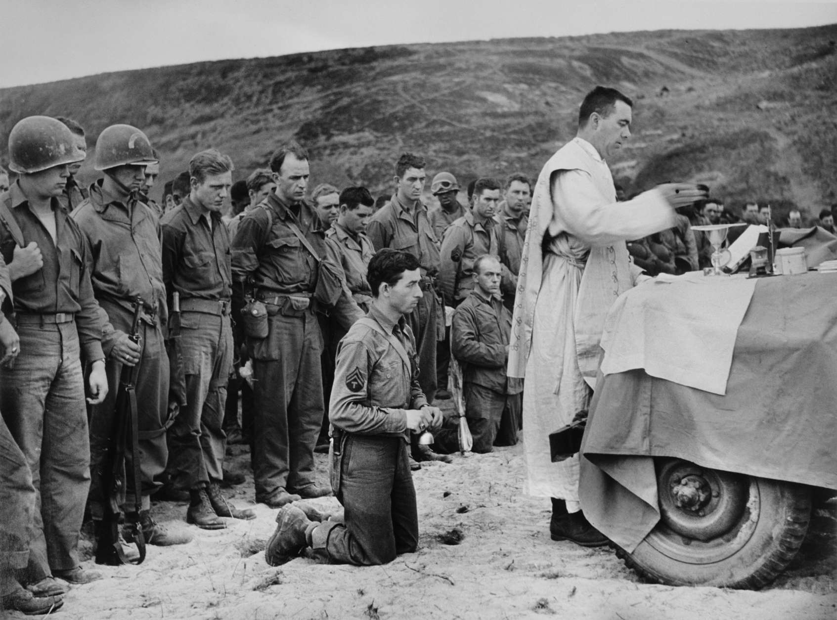 Robert Capa, [Using the hood of a jeep as an altar, a Roman Catholic chaplain saying mass at the inauguration of an American cemetery, Omaha Beach, Normandy], June 1944
©International Center of Photography/Magnum Photos  