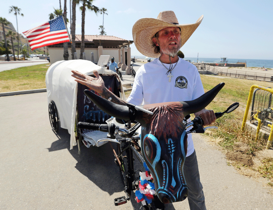 David Foute, 53, of Galveston, Texas, makes a stop on his months-long planned trek in honor of U.S. military veterans in a 'covered wagon,' which he tows on his bicycle, Sunday, May 28, 2017, at Will Rogers State Beach in the Pacific Palisades area of Los Angeles. Foute left Galveston on May 13, enroute to Oregon later this summer. "I'm not a veteran, but I'm trying to give back what they gave so much for us. I'm able to do what I'm doing because of them." (AP Photo/Reed Saxon)