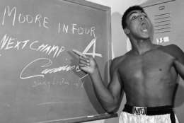 FILE - In this Nov. 15, 1962, file photo, young heavyweight boxer Cassius Clay, who later changed his name to Muhammad Ali,  points to a sign he wrote on a chalk board in his dressing room before his fight against Archie Moore in Los Angeles, predicting he'd knock Moore out in the fourth round, which he went on to do.  The sign also predicts Clay will be the next champ via a knockout over Sonny Liston in eight rounds. He did it in seven rounds. Ali turns 70 on Jan. 17, 2012. (AP Photo/Harold P. Matosian, File)