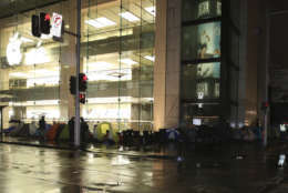 More than 50 people brave adverse weather conditions and camp on the street outside the Apple Store to be among the first to purchase the new iPhone 6s in Sydney, Australia, Friday, Sept. 25, 2015. The line stretched around the block and to the next street with people using tents, camp chairs and umbrellas to battle the rainy conditions. (AP Photo/Glenn Nicholls)
