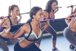 Beautiful young women with perfect bodies in sportswear exercising with barre while standing in front of window at gym