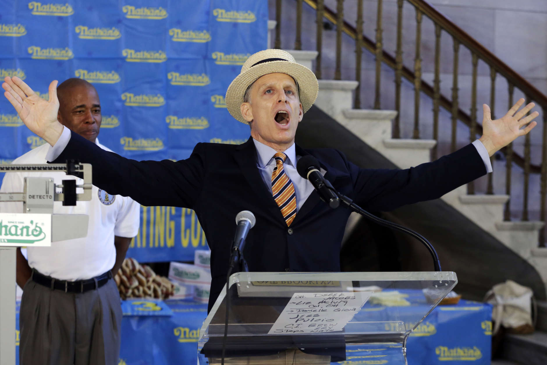 George Shea, master of ceremonies for the Nathan's Hot Dog Eating Contest, gives a sample of his introductions for the event, during the weigh-in for the 2017 contest , in Brooklyn Borough Hall, in New York, Monday, July 3, 2017. At left is Brooklyn Borough President Eric Adams. (AP Photo/Richard Drew)