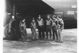 Plane crew assembles under wing of B-24.