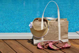 Beach bag with flip flops and a sun visor sitting on a pool deck
