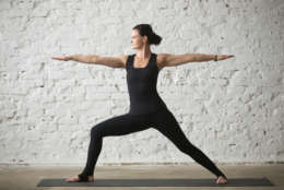 Young yogi attractive woman practicing yoga concept, standing in Warrior Two exercise, Virabhadrasana II pose, working out, wearing sportswear, black tank top and pants, full length, white loft