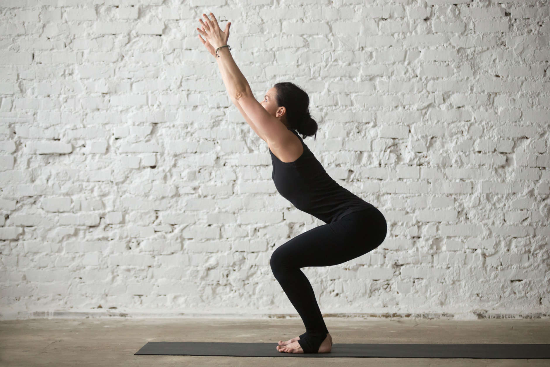 Young yogi attractive woman practicing yoga concept, doing advanced Chair exercise, Utkatasana pose, working out, wearing sportswear, black tank top and pants, full length, white loft background