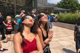 Two people at the Air and Space Museum in D.C. wear their protective glasses ahead of the eclipse. (WTOP/Megan Cloherty)