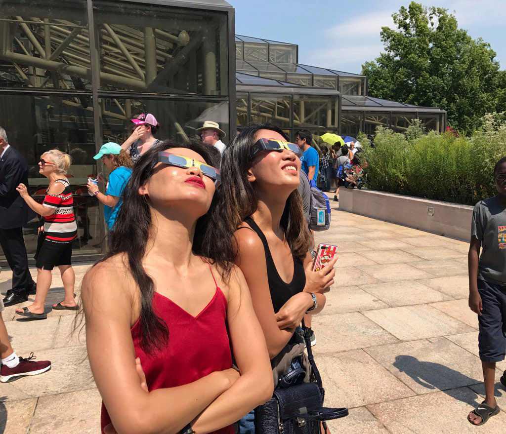 Two people at the Air and Space Museum in D.C. wear their protective glasses ahead of the eclipse. (WTOP/Megan Cloherty)
