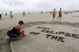 Val Carney, from Asheville, N.C., writes in the sand in preparation for the solar eclipse Monday, Aug. 21, 2017, on the beach at Isle of Palms, S.C. The city of Isle of Palms hosted a beach party "Get Eclipsed on IOP". (AP Photo/Mic Smith)