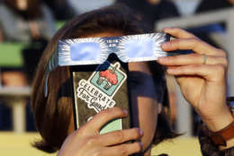 Catalina Gaitan, from Portland, Ore., tries to shoot a photo of the rising sun through her eclipse glasses at a gathering of eclipse viewers in Salem, Ore., Monday, Aug. 21, 2017. (AP Photo/Don Ryan)