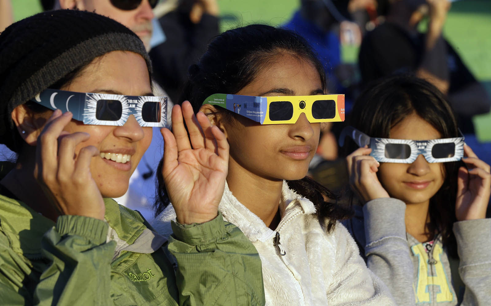 Schweta Kulkarni, from left, Rhea Kulkarni and Saanvi Kulkarni, from Seattle, try out their eclipse glasses on the sun at a gathering of eclipse viewers in Salem, Ore., early Monday, Aug. 21, 2017. (AP Photo/Don Ryan)