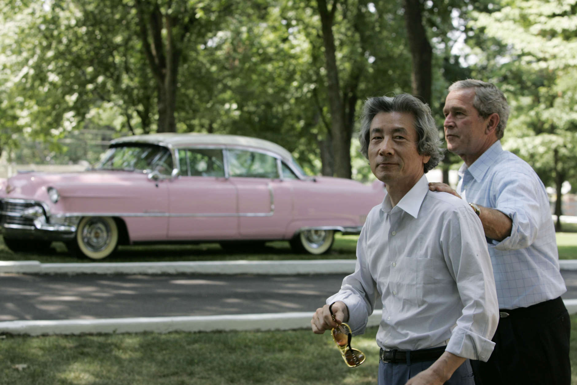 President Bush and Japanese Prime Minister Junichiro Koizumi, carrying a pair of Elvis style sunglasses, walk past Elvis' pink Cadillac after their tour of Graceland, the home of Elvis Presley, in Memphis, Tenn., Friday, June 30, 2006. (AP Photo/Charles Dharapak)