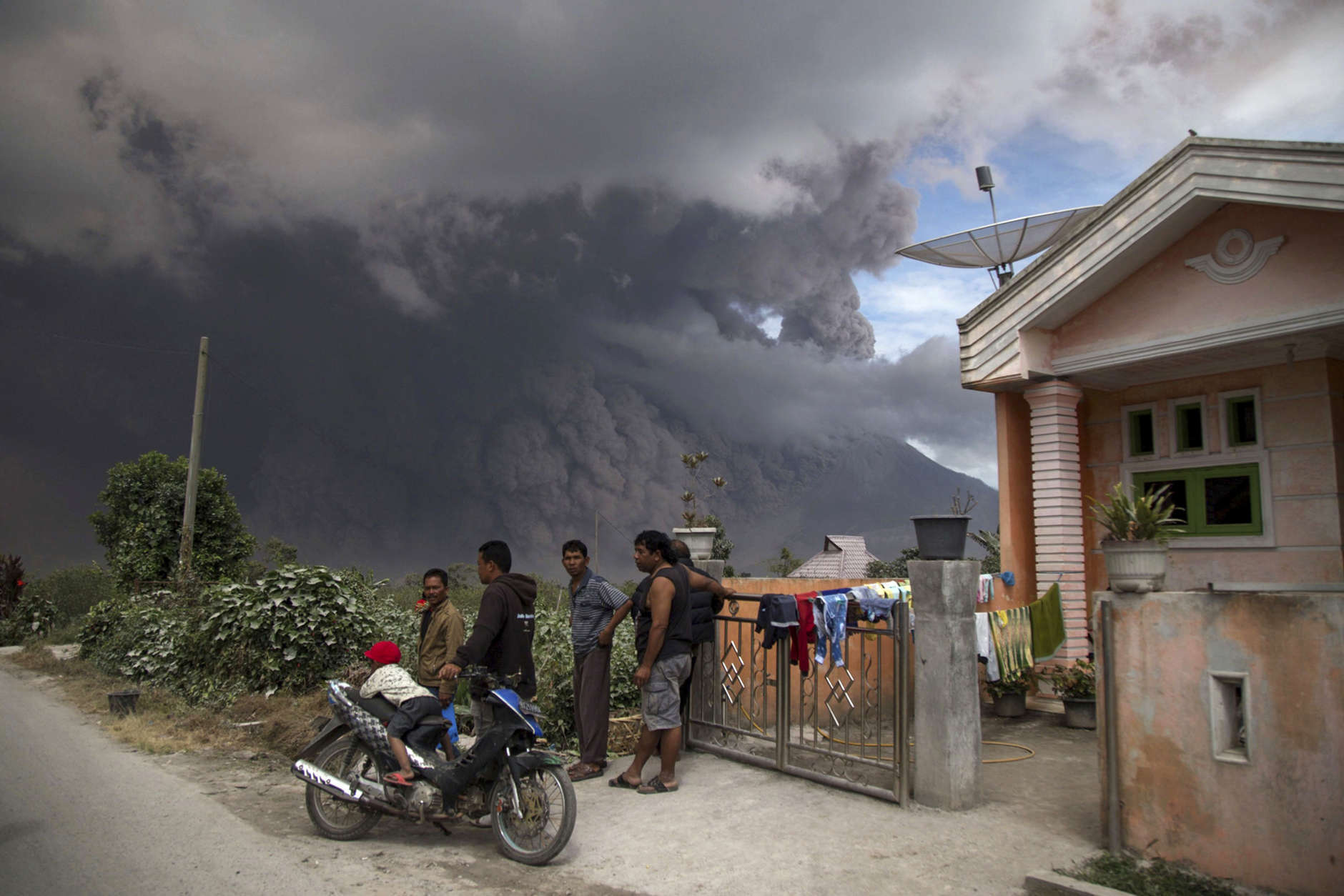 Villagers gather in front of a house as they watch Mount Sinabung releasing a pyroclastic flow during its eruption in Karo, North Sumatra, Indonesia, Wednesday, Aug. 2, 2017. The volcano blasted volcanic ash as high as 4.2 kilometers (2.6 miles), one of its biggest eruptions in the past several months of high activity. (AP Photo/Endro Rusharyanto)