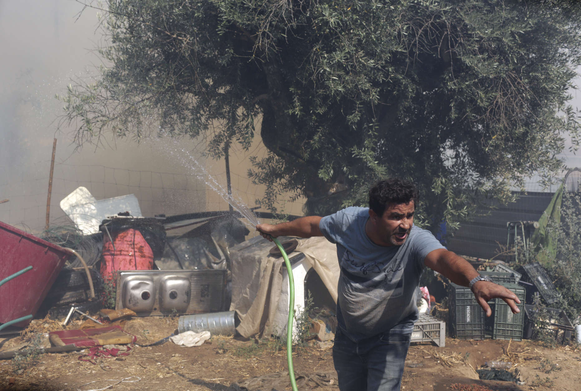 A man holding a garden hose shouts to someone as flames from a wildfire reach the backyard of a house in the town of Macao, central Portugal, Thursday, Aug. 17 2017. Portugal's government is taking the rare step of decreeing a state of public calamity ahead of a forecast rise in temperatures that authorities fear will worsen a spate of wildfires. (AP Photo/Armando Franca)