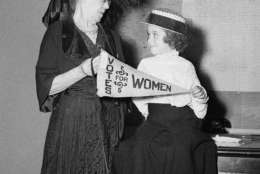 Comparing notes in Chicago on Aug. 6, 1948, are Margaretta Helm, six-year-old suffragette from Evanston Ill., and Dr. Anna R. Ranes, who was a delegate to the last national American womans suffrage meeting. Dr. Ranes is showing the banner she carried at the convention to Margarette who wears the slightly oversized costume in which she will appear in a pageant celebrating the 28th anniversary of womens suffrage. (AP Photo/Edward Kitch)