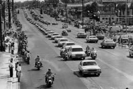 A string of white vehicles follow the hearse carrying the body of rock and roll musician Elvis Presley along Elvis Presley Boulevard on the way to Forest Hills Cemetery in Memphis, Tenn., Aug. 19, 1977.  Thousands of people line the route for the city's final tribute to Elvis.  (AP Photo)