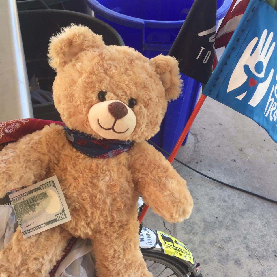 Miles, a teddy bear the cyclist’s mom gave him, holds $100 on April 28, donated by what the 24-year-old calls a “road angel.” (Courtesy of Spencer Buchness)