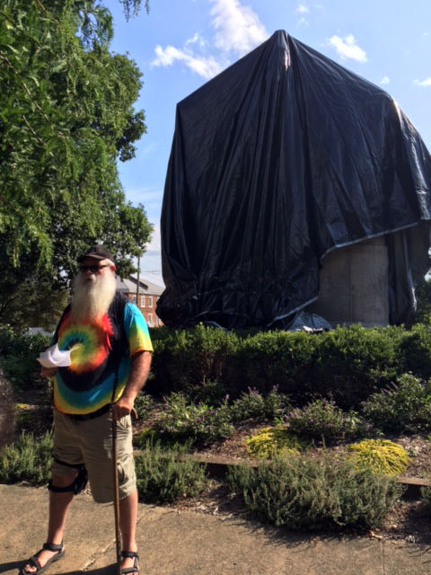John Miska, a veteran and self-proclaimed free-speech advocate wearing a tie-die T-shirt and carrying a legal weapon, cut away a small section of the black tarp before Charlottesville police ordered him stop Wednesday. (WTOP/Shawn Anderson)