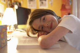 Girl (6-8) resting head on book, smiling, portrait