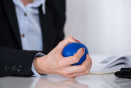 Close-up Of Businessperson Hand Squeezing Blue Stressball In Hand At Desk