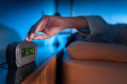 Woman pressing snooze button on early morning digital alarm clock (Thinkstock)