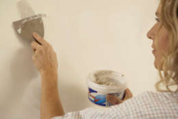 Woman filling hole in wall with multi-purpose filler, close-up