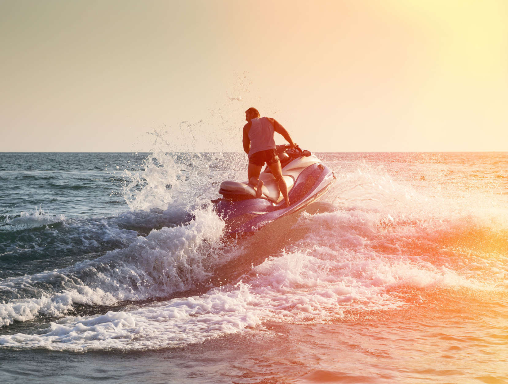 Silhouette of strong man jumps on the jetski above the water at sunset