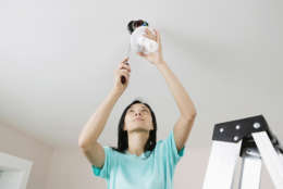 Low angle view of a young woman fixing a light fixture