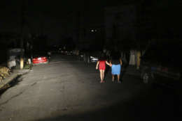 Raphael Urena and Viviana Urena, illuminated by the headlights from a car, walk down a residential street, as most of Puerto Rico copes without electricity, in the aftermath of Hurricane Maria in San Juan, Puerto Rico, Wednesday, Sept. 27, 2017. (AP Photo/Gerald Herbert)