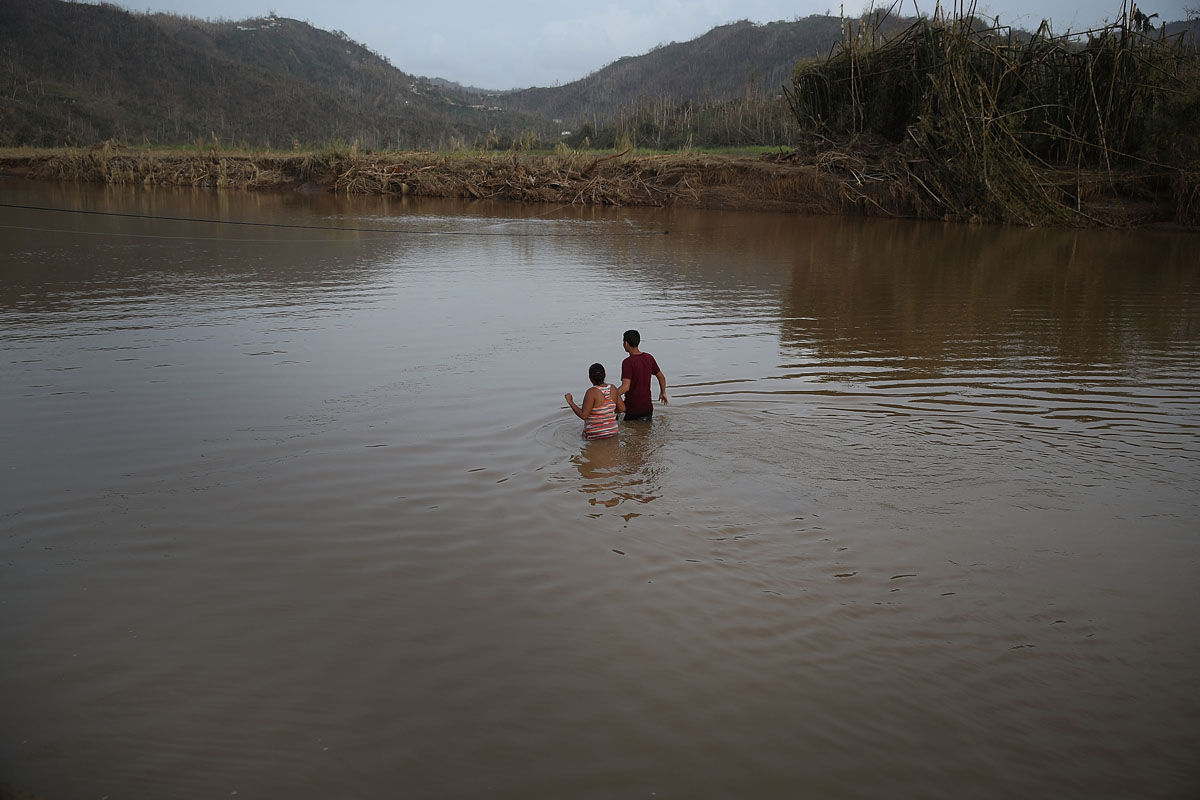 MOROVIS, PUERTO RICO - SEPTEMBER 27:  Hector Ojeda and Sonia Robles and Tony Ojeda cross a river on foot after the bridge was washed away when Hurricane Maria passed through on September 27, 2017 in Morovis, Puerto Rico.  Puerto Rico experienced widespread damage including most of the electrical, gas and water grid as well as agriculture after Hurricane Maria, a category 4 hurricane, passed through.  (Photo by Joe Raedle/Getty Images)