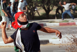 A man with the Palestinian flag wrapped around his head, throws stones during clashes between Paletinians and Israeli soldiers at the entrance of Israeli Netzarim Jewish settlement crossing, in the southern Gaza City, Saturday, Sept. 30, 2000.  Palestinian youths stoned Israelis a day after Israel riot police stormed a major Muslim shrine in Jerusalem killing  six Palestinians. (AP Photo/Adel Hana)