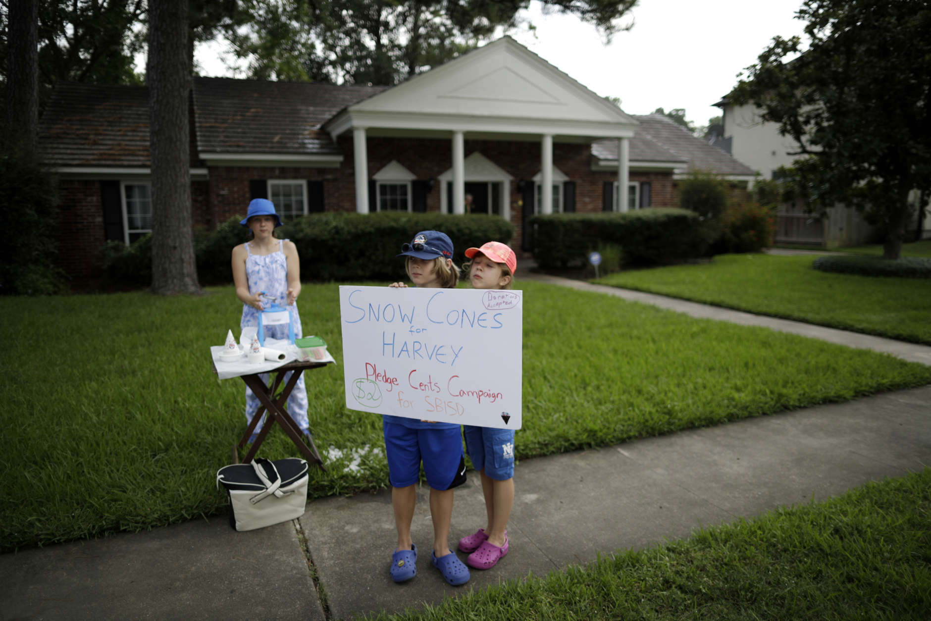 Leonard Olschimke, center, holds a sign offering snow cones as he stands in front of his house with sisters Sarah, right, and Lily, left, Friday, Sept. 1, 2017, in Houston. Thousands of people have been displaced by torrential rains and catastrophic flooding since Harvey slammed into Southeast Texas last Friday. (AP Photo/Gregory Bull)