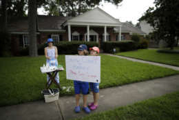 Leonard Olschimke, center, holds a sign offering snow cones as he stands in front of his house with sisters Sarah, right, and Lily, left, Friday, Sept. 1, 2017, in Houston. Thousands of people have been displaced by torrential rains and catastrophic flooding since Harvey slammed into Southeast Texas last Friday. (AP Photo/Gregory Bull)