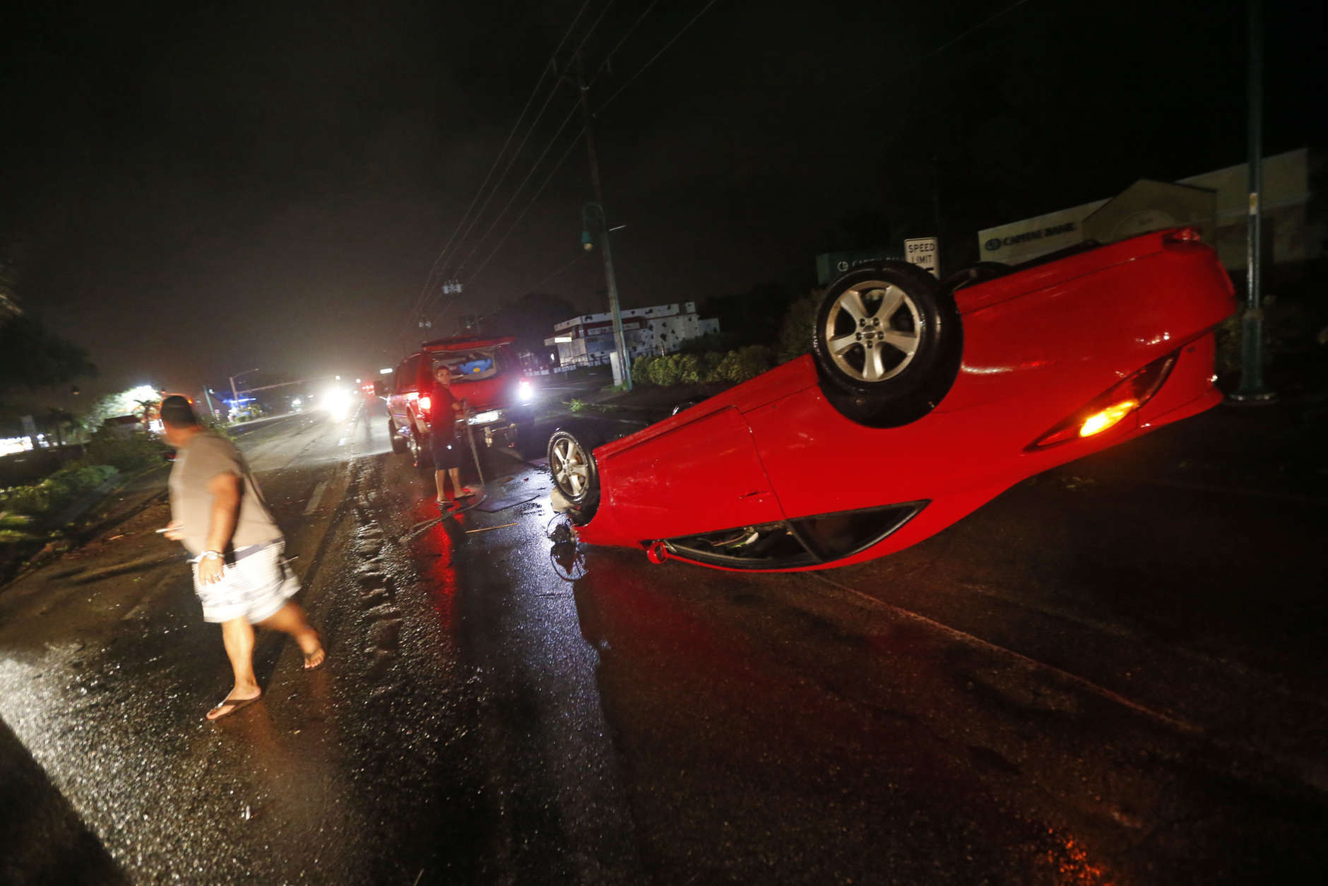 People tend to a car that flipped over on Cape Coral Parkway during Hurricane Irma, in Cape Coral, Fla., Sunday, Sept. 10, 2017. (AP Photo/Gerald Herbert)