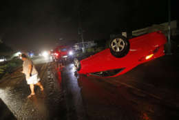 People tend to a car that flipped over on Cape Coral Parkway during Hurricane Irma, in Cape Coral, Fla., Sunday, Sept. 10, 2017. (AP Photo/Gerald Herbert)
