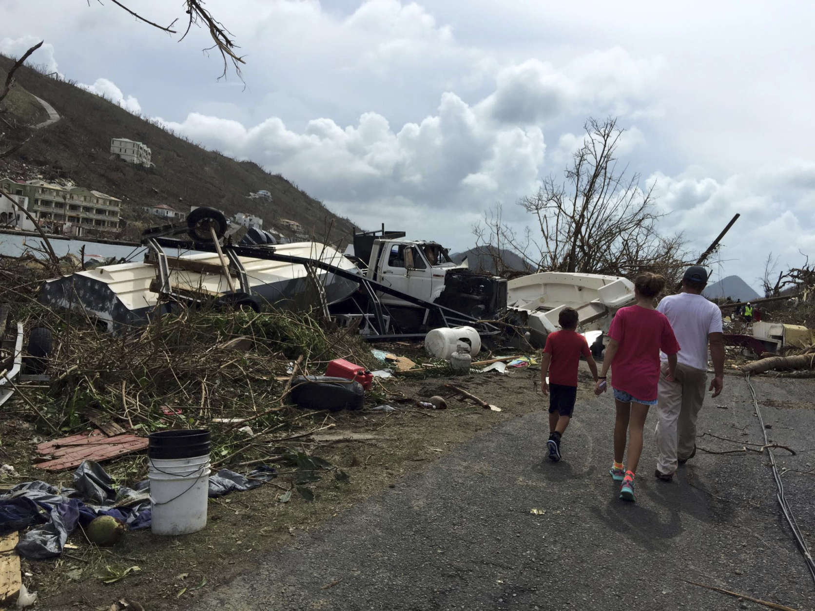 In this Sept. 8, 2017 photo, people walk near debris in the aftermath of Hurricane Irma in Tortola, in the British Virgin Islands. Britain has sent a navy ship and troops to help people on the British Virgin Islands, Anguilla and the Turks and Caicos islands that were pummeled by the hurricane. (Gabi Gonzalez via AP)