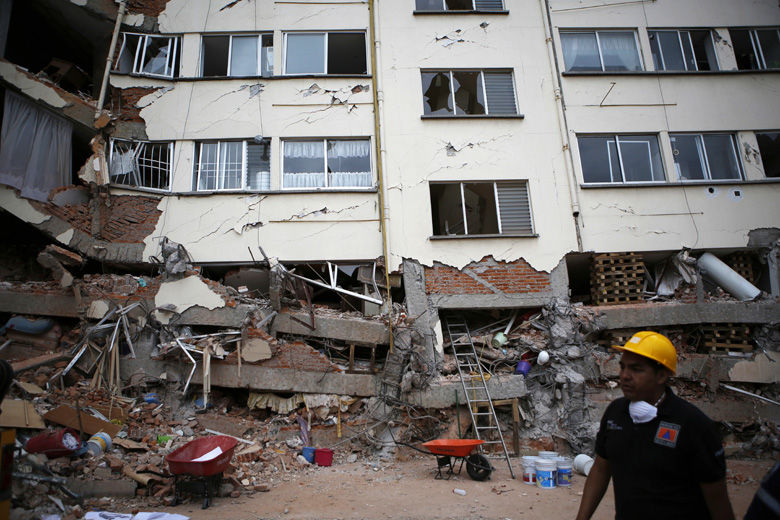 A rescue worker walks in front of an apartment building whose first four floors collapsed, in the Lindavista neighborhood of Mexico City, Wednesday, Sept. 20, 2017. People by the millions rushed from homes and offices across central Mexico, after a 7.1 earthquake, sometimes watching as buildings they had just fled fell behind them with an eruption of dust and debris. (AP Photo/Rebecca Blackwell)