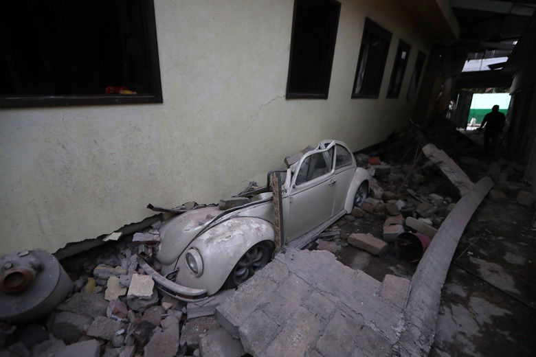 In this Sept. 20, 2017 photo, a car sits crushed from a building felled by a 7.1 earthquake, in Jojutla, Morelos state, Mexico. Efforts continue at the scenes of dozens of collapsed buildings, where firefighters, police, soldiers and civilians continue their search to reach the living. (AP Photo/Eduardo Verdugo)
