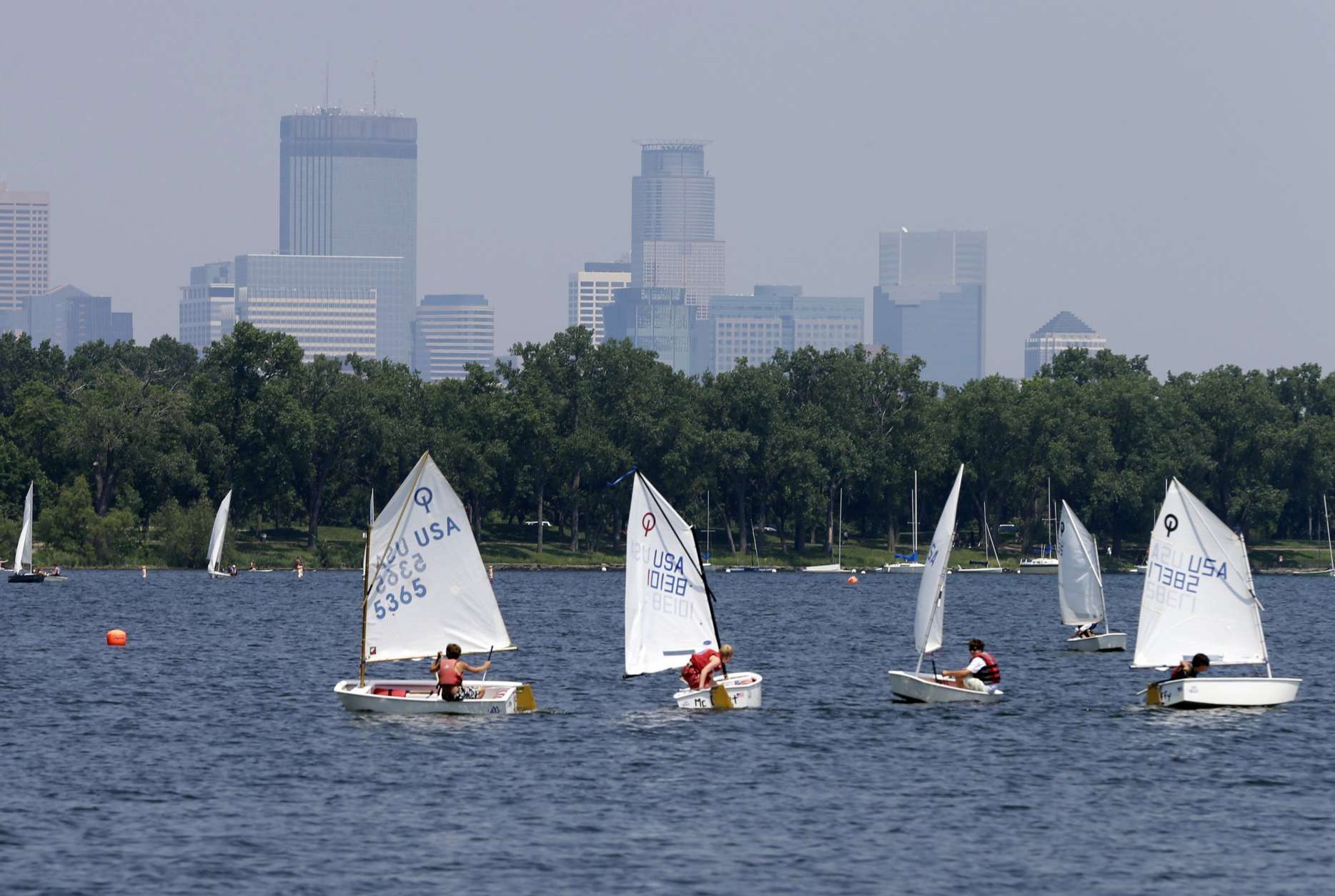 Sailing enthusiasts navigate the waters of Lake Calhoun as the Minneapolis skyline rises, shrouded in hazy skies because of elevated levels of fine particle pollution, likely the result of smoke from Canadian forest fires,Thursday, July 11, 2013. Air pollution levels are expected to remain elevated through Friday evening, July 12.  (AP Photo/Jim Mone)
