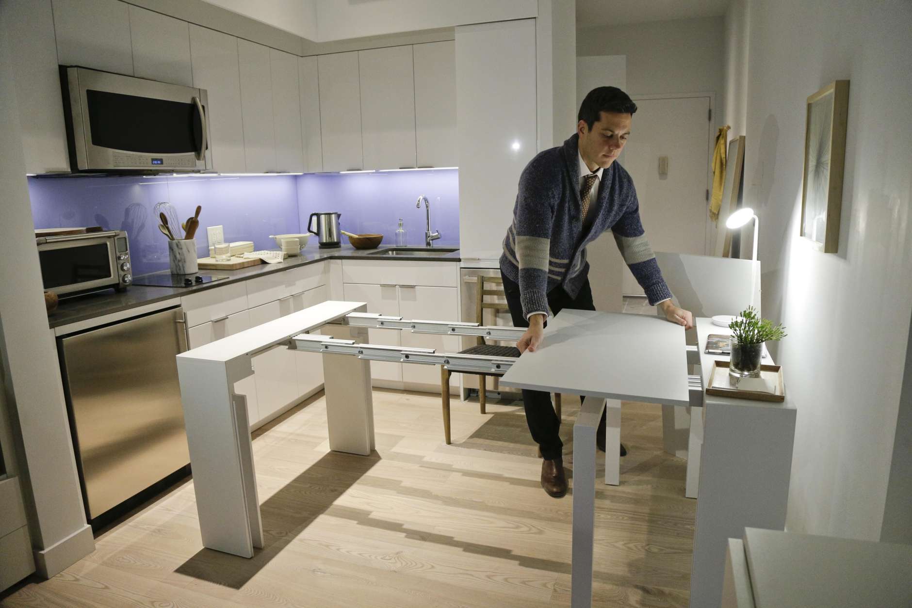 In this Dec. 22, 2015, photo, Stage 3 Properties co-founder Christopher Bledsoe demonstrates a desk that expands into a dining table that can seat up to 12 people inside one of the apartments at the Carmel Place building in New York. As the city-sponsored micro-apartment project nears completion, its setting an example for tiny dwellings that the nations biggest city sees as an aid to easing its affordable housing crunch. (AP Photo/Julie Jacobson)