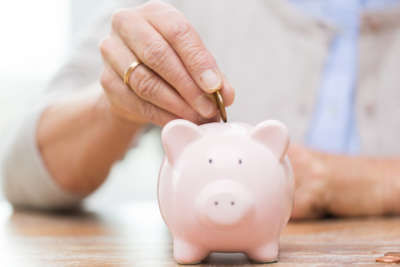 savings, money, annuity insurance, retirement and people concept - close up of senior woman hand putting coin into piggy bank